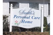 A white wooden sign reading "Smith's Personal Care Home" mounted on posts in front of a white building.