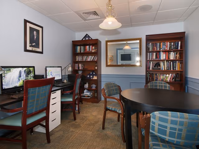 Small communal study room with bookshelves, computer workstations, a round table and upholstered chairs.
