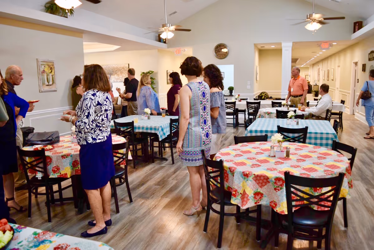 Residents and visitors mingling in a dining room with round tables covered in colorful tablecloths.