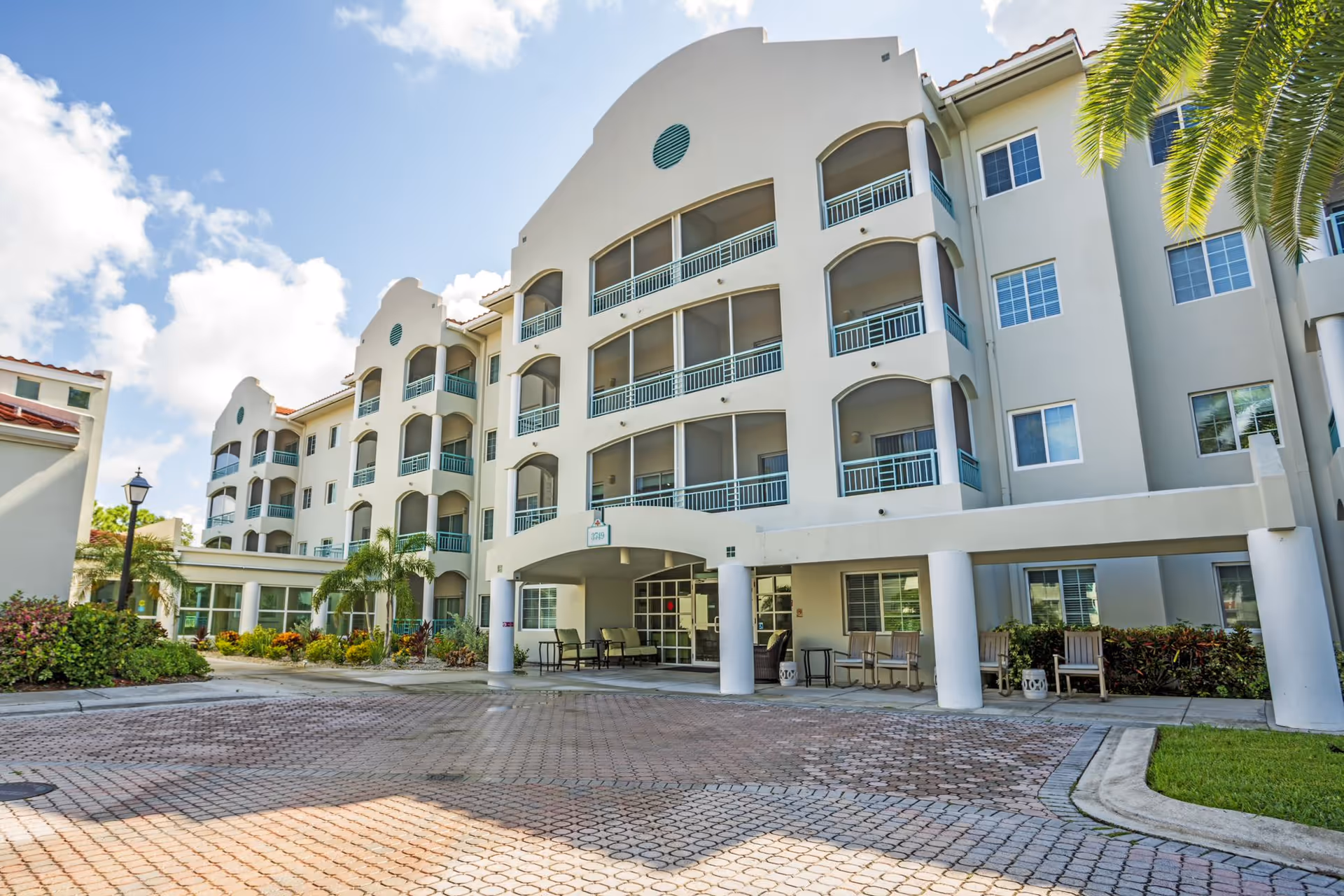 Exterior view of a multi-story senior living building with balconies and palm trees.