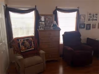 Cozy living room with two chairs, a dresser, windows, and a photo gallery.