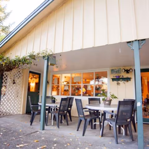 Outdoor patio with tables and chairs under a beige awning beside a glass-windowed building.