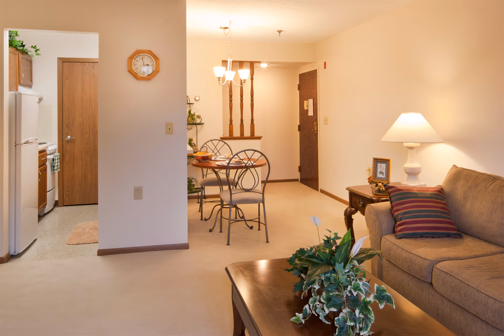 Cozy living room and dining area with a sofa, coffee table with plants, a small dining table, and a view into the kitchen.