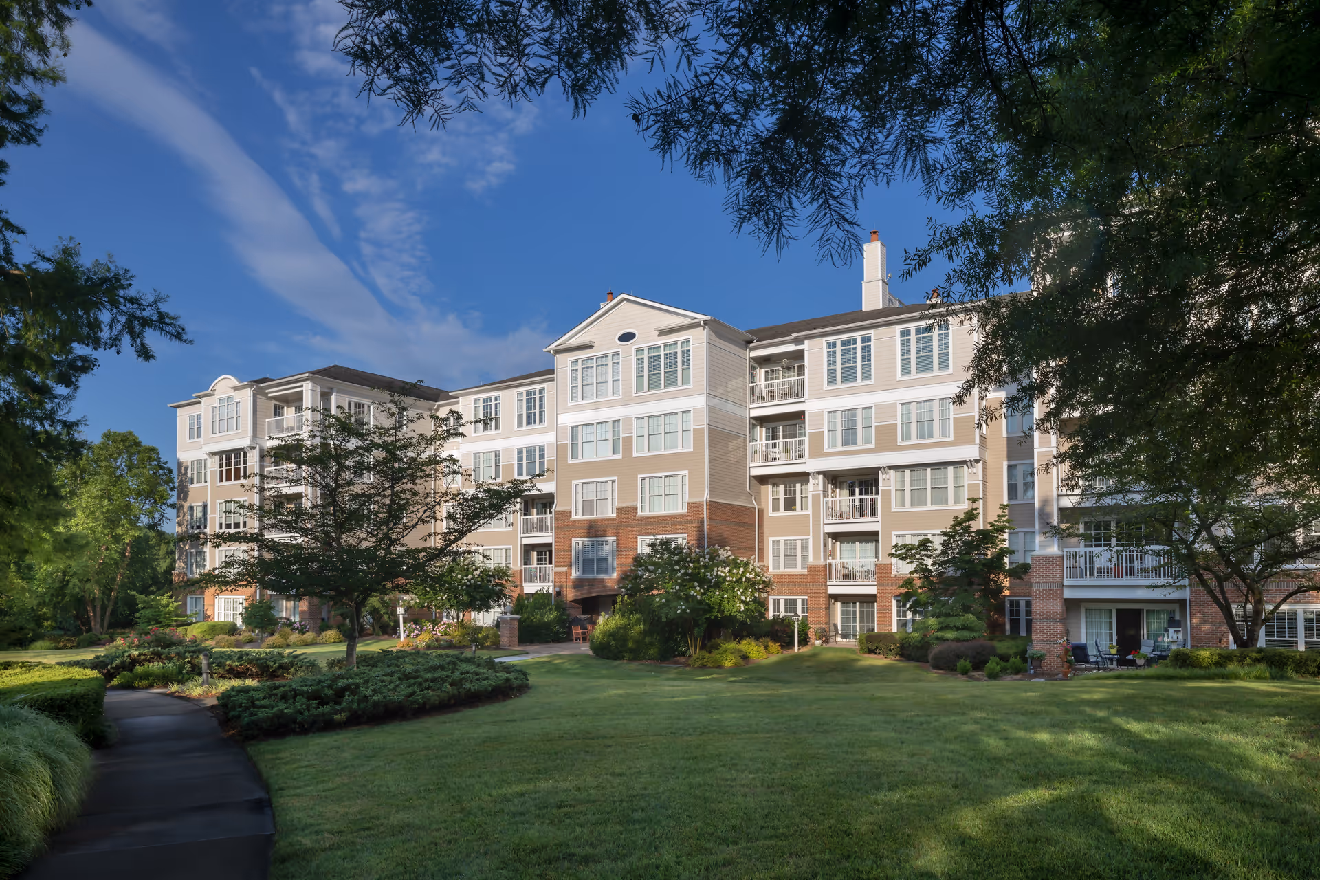 Front exterior view of a multi-story senior living building with balconies and landscaped lawn.