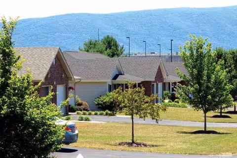 One-story senior living center with shrubs, trees, and a parking lot in front.