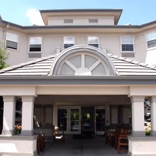 Front exterior view of Belleview Suites at DTC building with a covered entrance supported by columns, outdoor seating, and multiple windows under a partly cloudy sky.