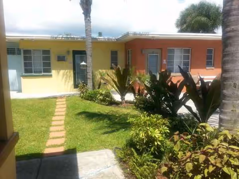 A sunny courtyard with a grassy lawn, stepping-stone path, and colorful building fronts.