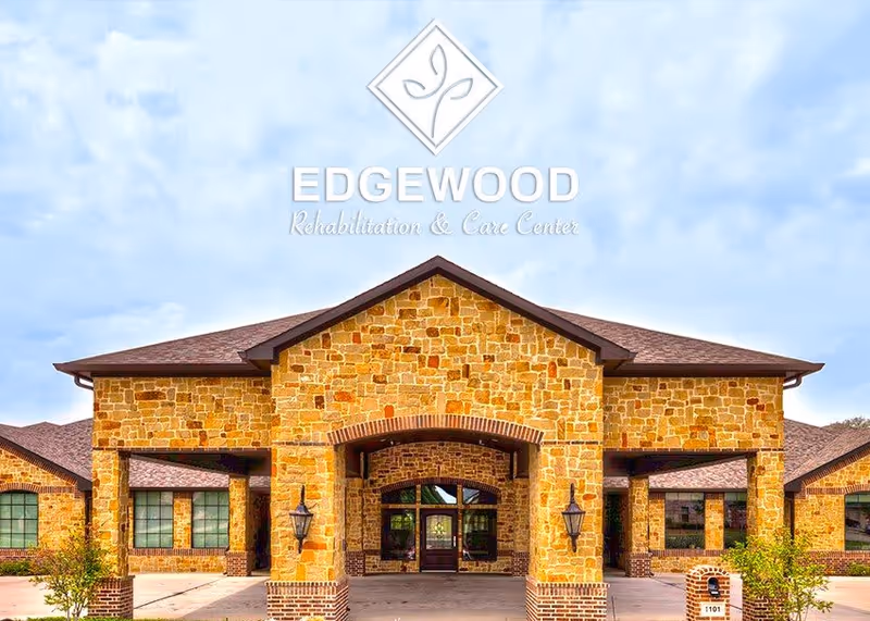 Front exterior view of a stone building with a peaked roof and large entrance, under a partly cloudy sky. The building has multiple windows and outdoor lamps on either side of the entrance.