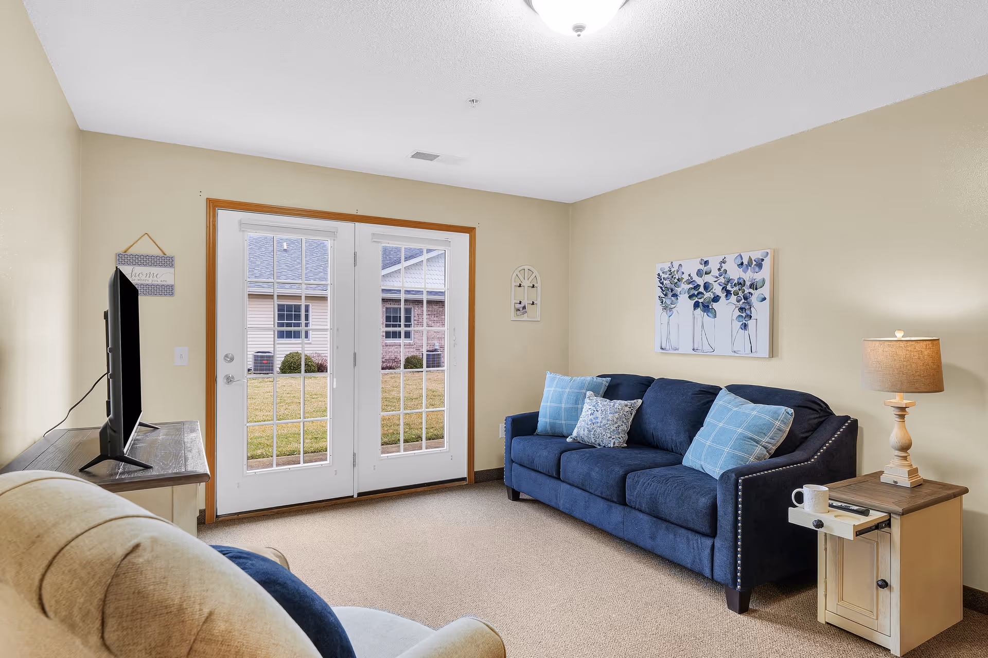 Cozy living room with blue sofa, beige walls, and French doors to outdoors.