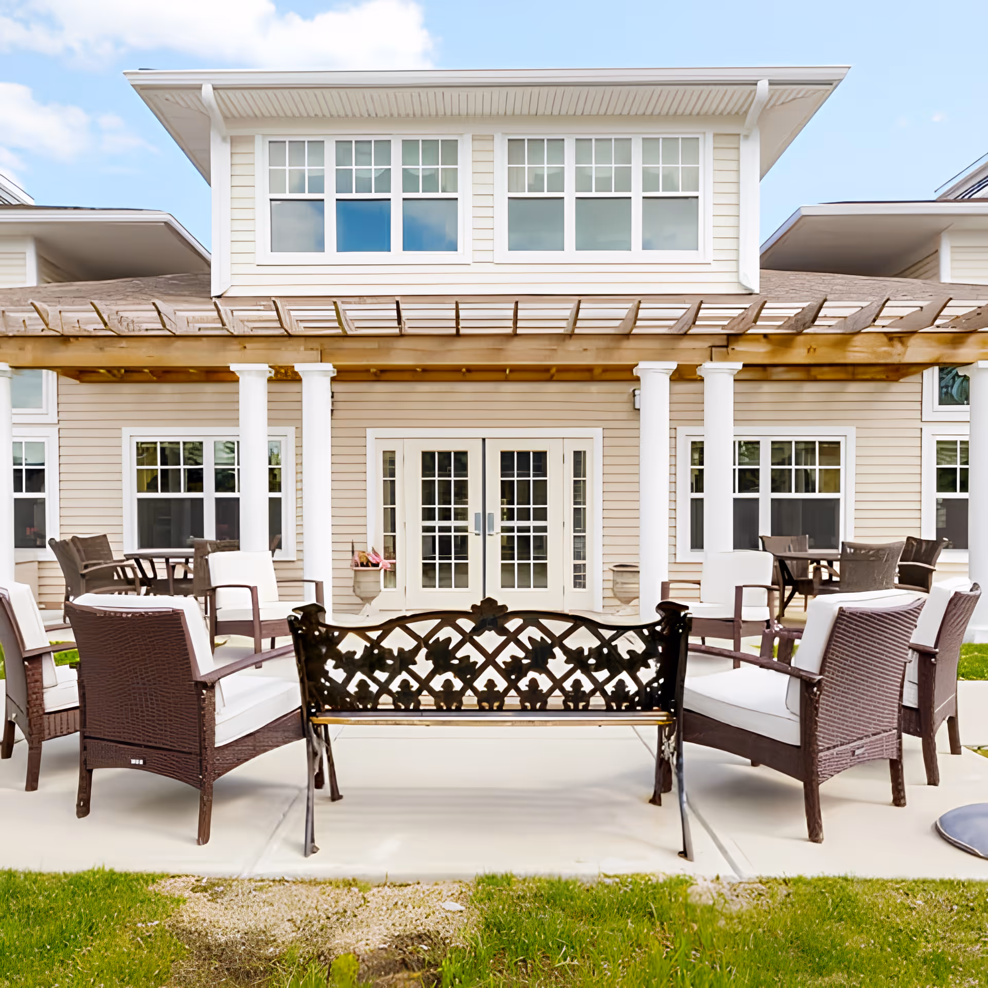 Outdoor patio with chairs and a decorative bench in front of a two-story building with French doors and a pergola.