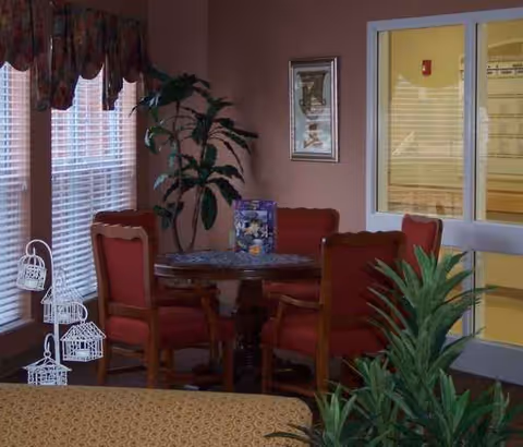 Indoor dining area with red upholstered chairs around a round wooden table and plants.