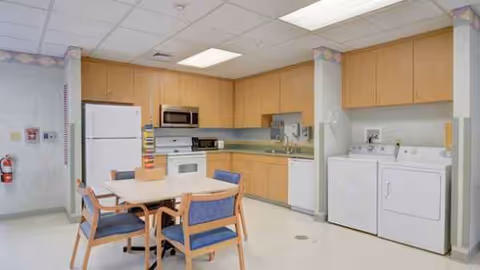Bright kitchen and dining area in a senior living facility with appliances and table.