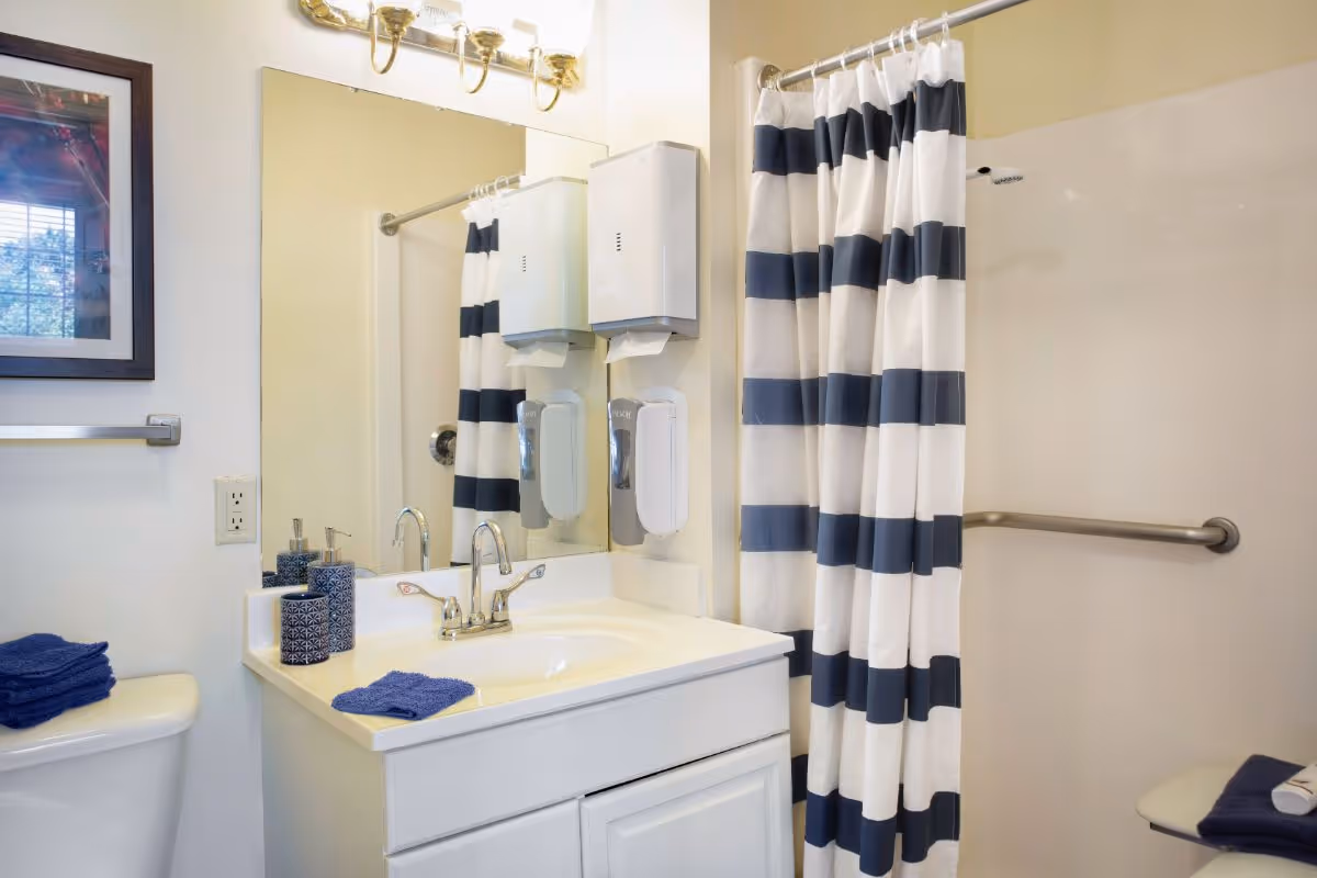 A bright bathroom with a vanity, mirror and sink, a navy-and-white striped shower curtain, grab bar and folded towels.