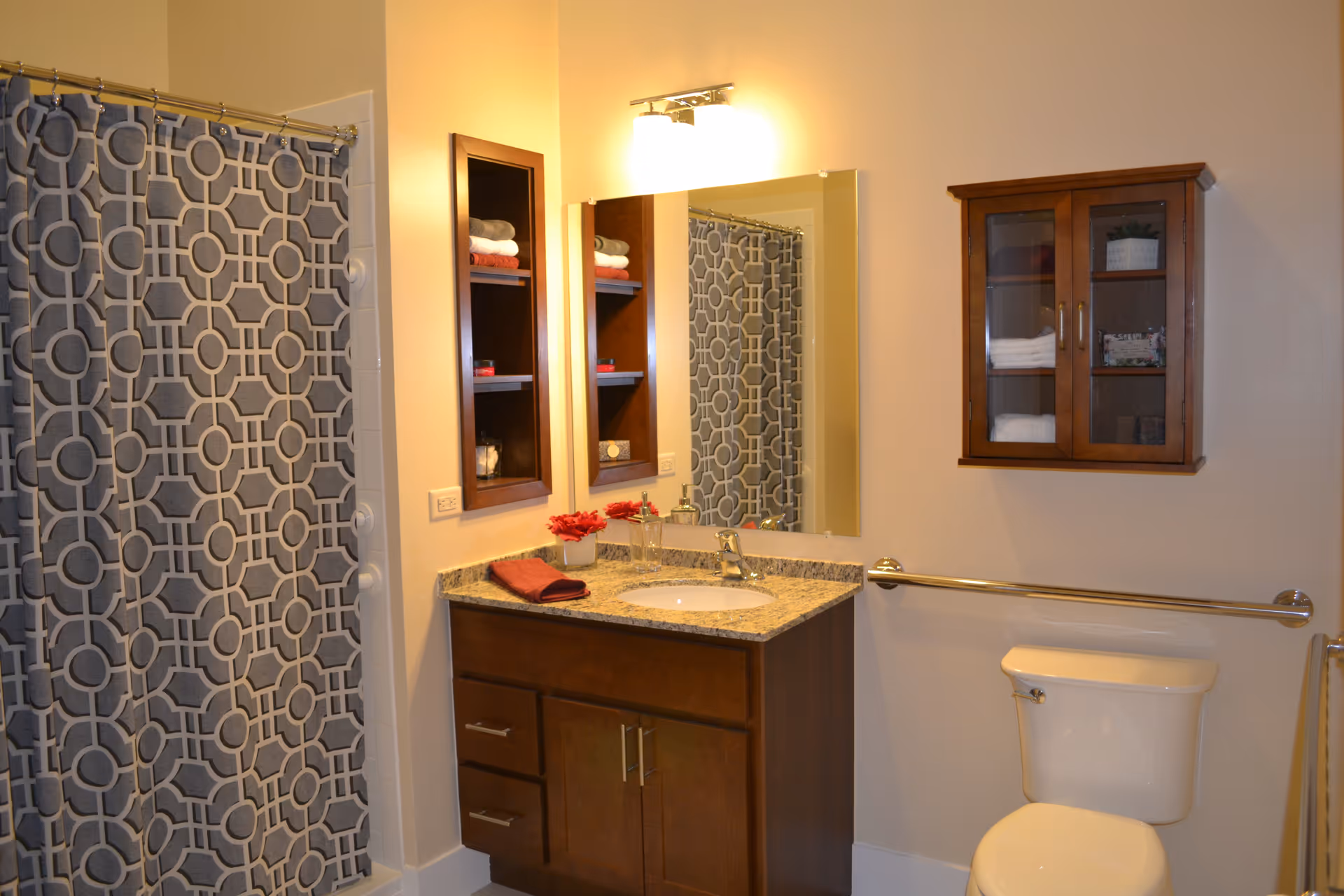 Bathroom interior featuring a vanity with sink and mirror, patterned shower curtain, wall cabinets, and a toilet.