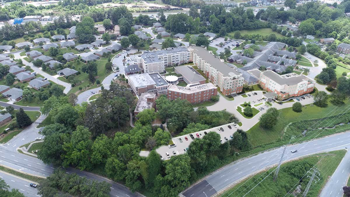 Aerial view of the WhiteStone senior living campus with multi-story buildings, parking lots, surrounding trees, neighboring homes, and nearby roads.