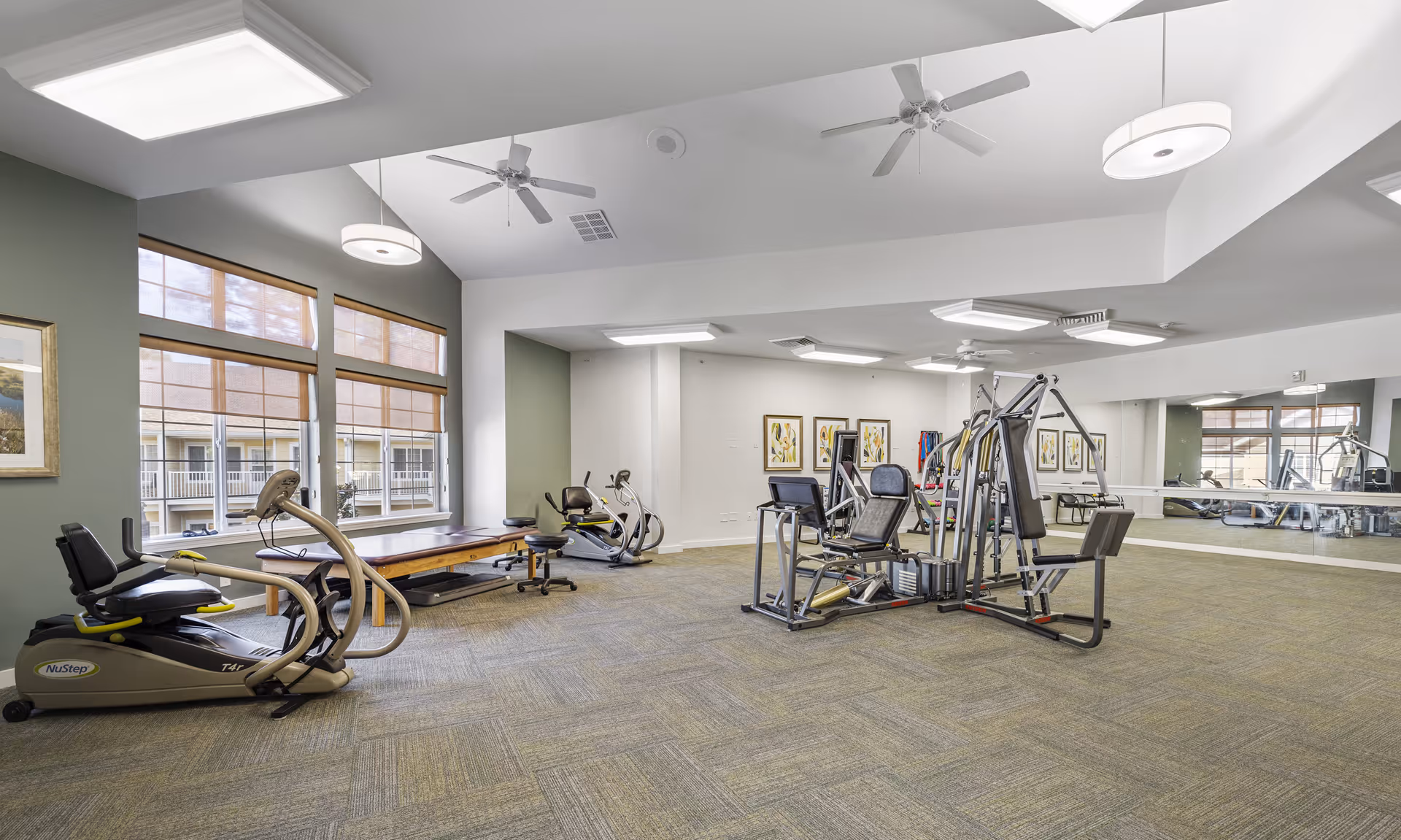 Bright fitness room with exercise machines, weight equipment, large windows and wall mirrors.
