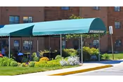 Green entrance awning over a landscaped walkway in front of a brick apartment building.