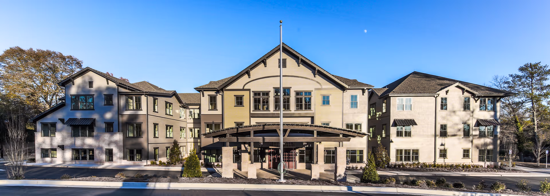 Front exterior of a three-story senior living building with a covered entrance and central flagpole.