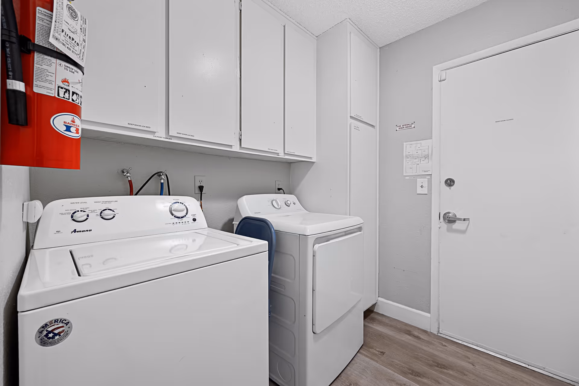 Small laundry room with a washer and dryer, white cabinets, and a fire extinguisher on the wall.