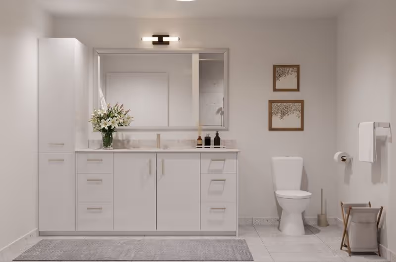A clean and modern bathroom featuring a white vanity with multiple drawers and cabinets, a large mirror above the sink, a vase with white flowers on the countertop, a toilet, two framed pictures on the wall, a towel rack with a white towel, a toilet paper holder, and a small laundry basket on the floor.