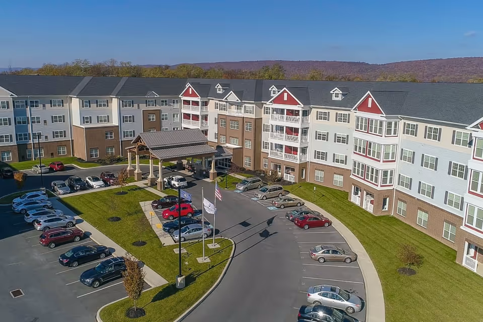 Aerial view of the multi-story Harmony at West Shore building with a covered entrance, flagpoles and a surrounding parking lot.