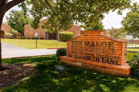 Exterior view of The Manor at Seagoville with a brick sign and trees.
