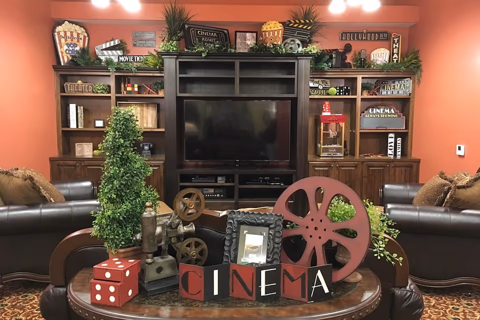 Movie-themed common room with a large TV in a dark wood entertainment center, leather sofas, and decorative film reels and popcorn props.