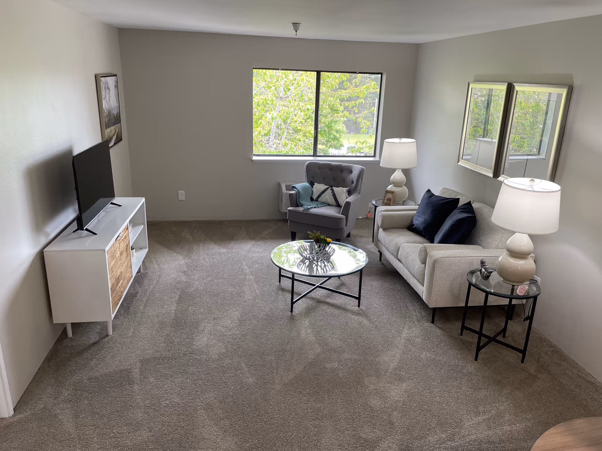 Bright living room in a senior facility with sofa, chairs, coffee table, and a TV.