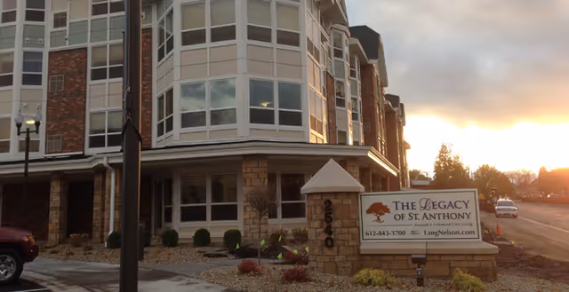 Front exterior of a multi-story senior living building at sunset with a stone sign reading 'The Legacy of St. Anthony'.
