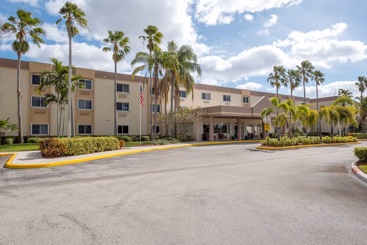 Front exterior of a three-story senior living building with palm trees, a covered entrance, and a circular driveway.