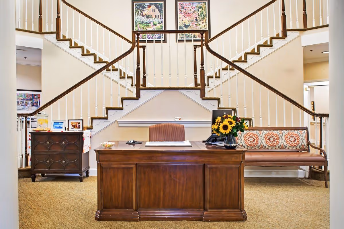Lobby reception area with a wooden front desk, sunflower arrangement, bench seating, and a split staircase behind.