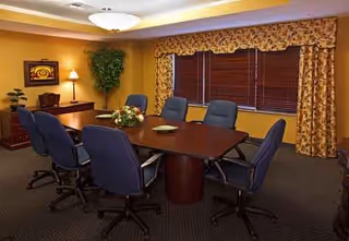 A meeting room in a senior living facility with a long wooden table and blue chairs.