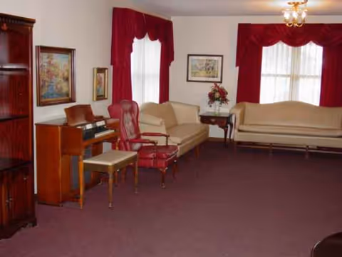 Traditional living room with beige sofas, red curtains, a piano, and framed artwork.