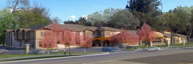 Front view of a two-story residential building set behind ornamental trees with a street and cars in the foreground.