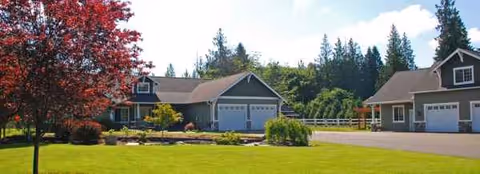 Exterior view of a senior living facility with green lawn, trees, and connected beige garages.