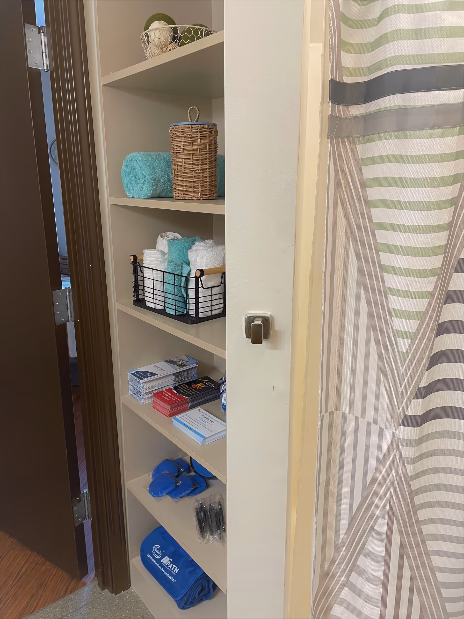 Built-in bathroom shelving stocked with towels, baskets, brochures and amenities next to a striped shower curtain.