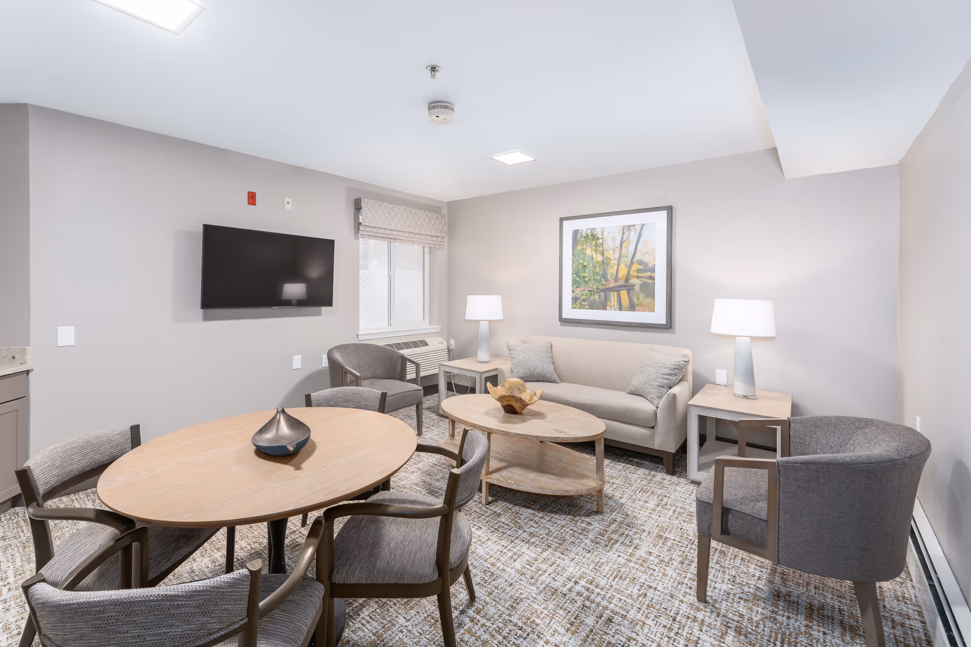 Bright furnished sitting room with a sofa, armchairs, coffee table, round dining table and wall-mounted TV.