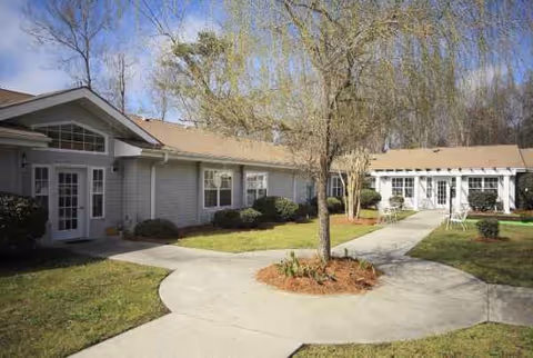 Cypress Square senior living exterior with a curved concrete walkway and trees.