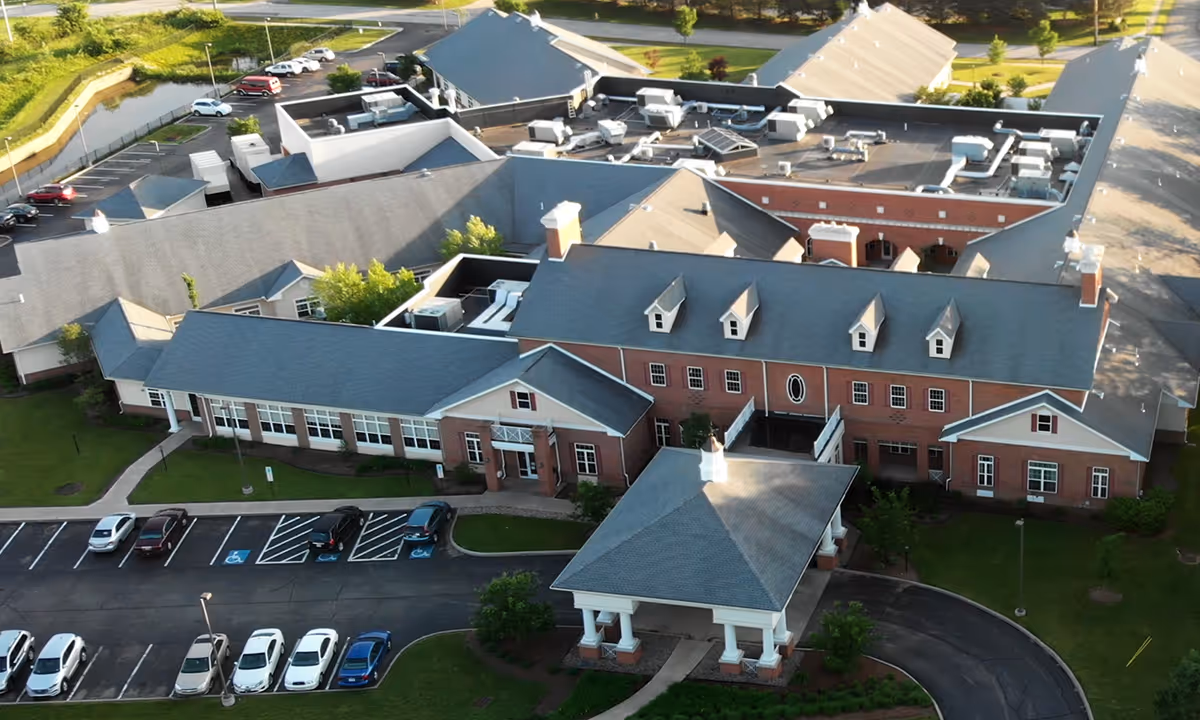 Aerial view of a brick nursing and rehabilitation facility with a covered porte-cochère entrance, parking lot, and rooftop HVAC units.