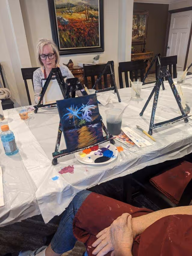 Residents painting at a table with easels and art supplies in a communal indoor room.