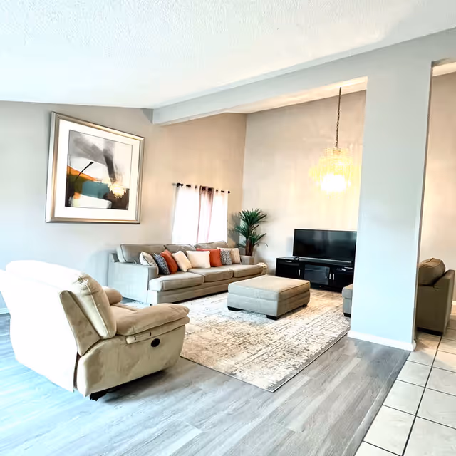 Bright, spacious living room with sofa, recliner, coffee ottoman, TV, and chandelier.