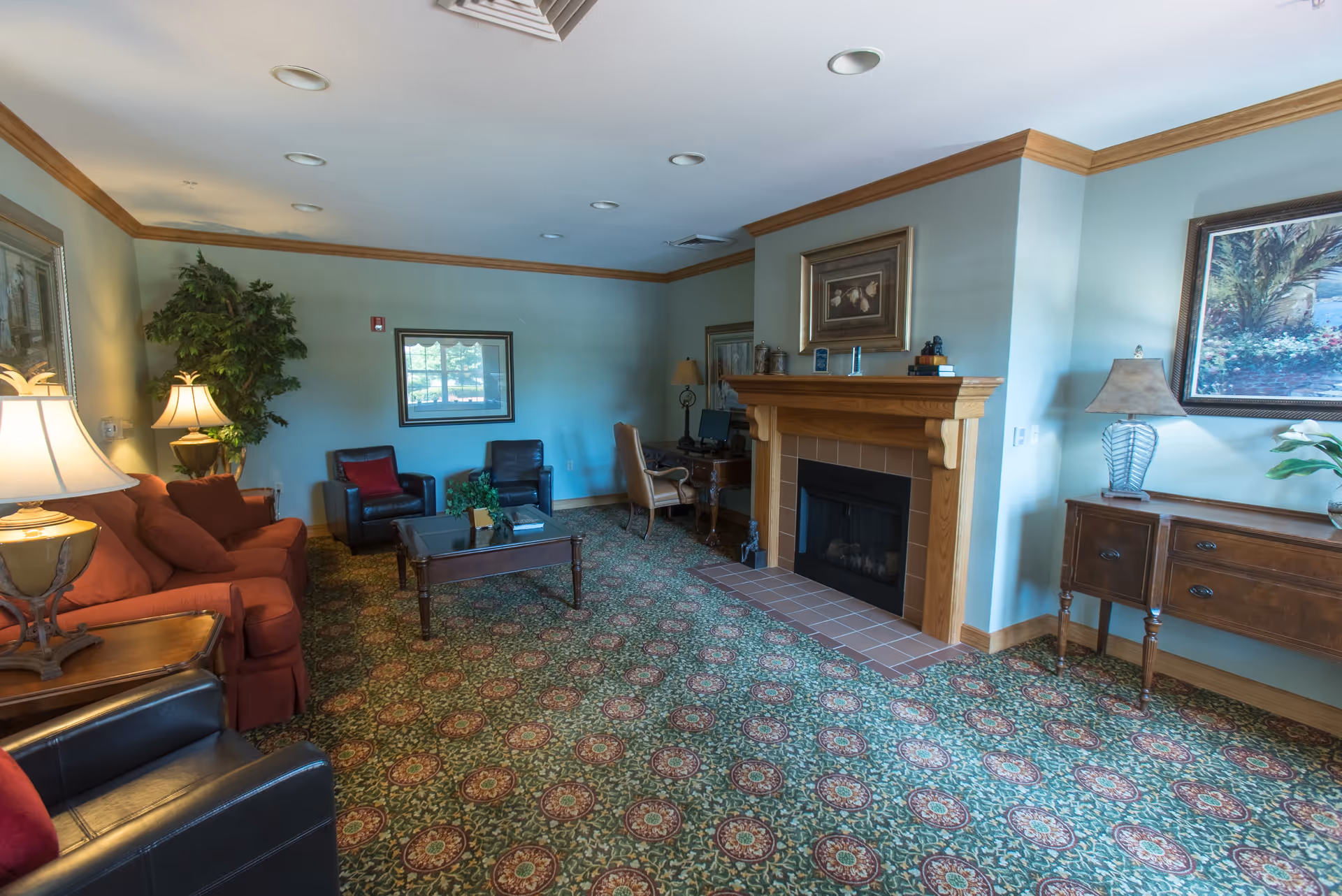 Comfortable living room with sofas and armchairs arranged around a coffee table in front of a fireplace, accented by lamps, artwork, and patterned carpet.