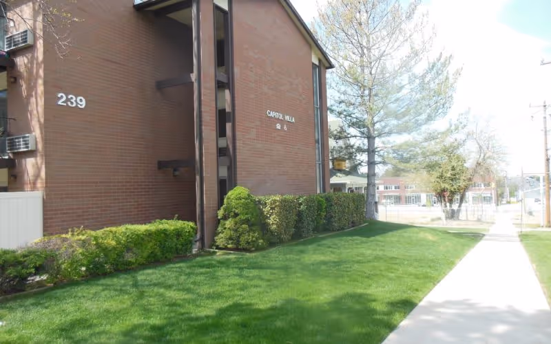 Capitol Villa brick building with a manicured lawn, hedges, and a sidewalk.