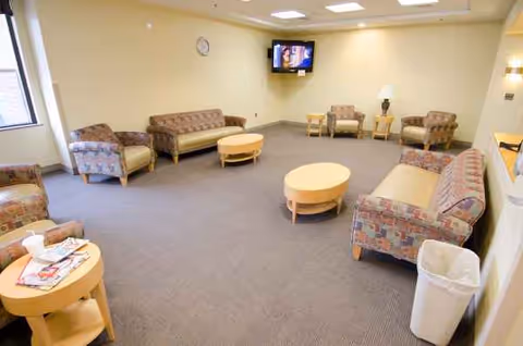 A spacious, well-lit lounge with several sofas, tables, and a wall-mounted TV.
