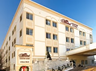 Exterior view of The Bristal Assisted Living at Lynbrook building, showing a multi-story beige and cream facade with multiple windows and a covered entrance area.