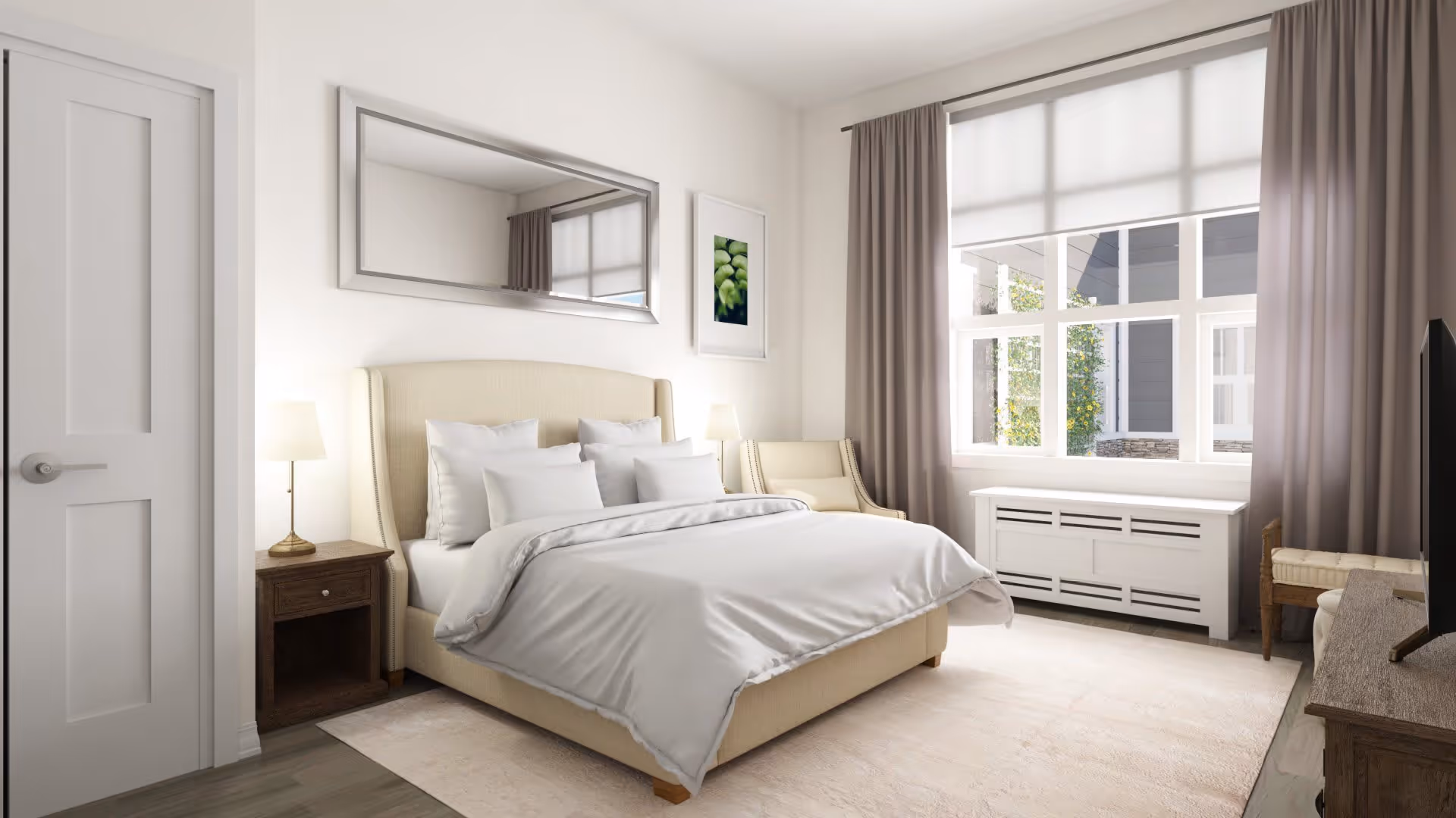 A bright and cozy bedroom with a beige upholstered bed neatly made with white bedding and multiple pillows. There is a wooden nightstand with a lamp on the left side of the bed and a beige armchair next to it. A large window with white blinds and beige curtains lets in natural light. A white radiator cover is beneath the window, and a wooden dresser with a TV on top is on the right side. The walls are white with a large rectangular mirror and a framed picture hanging above the bed.