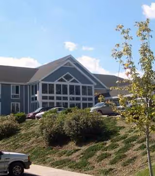 Front exterior of a senior living facility with parked cars and landscaped hillside.