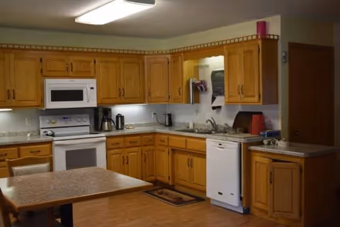 Wooden kitchen cabinets surround a standard kitchen with stove, microwave, sink, and dishwasher.