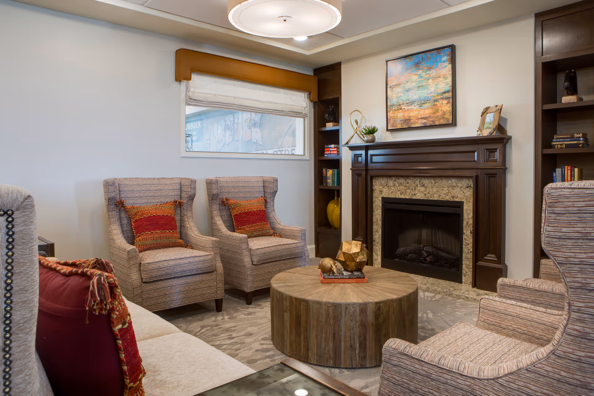 Cozy living room with upholstered armchairs around a round wooden coffee table and a fireplace with built-in shelving.