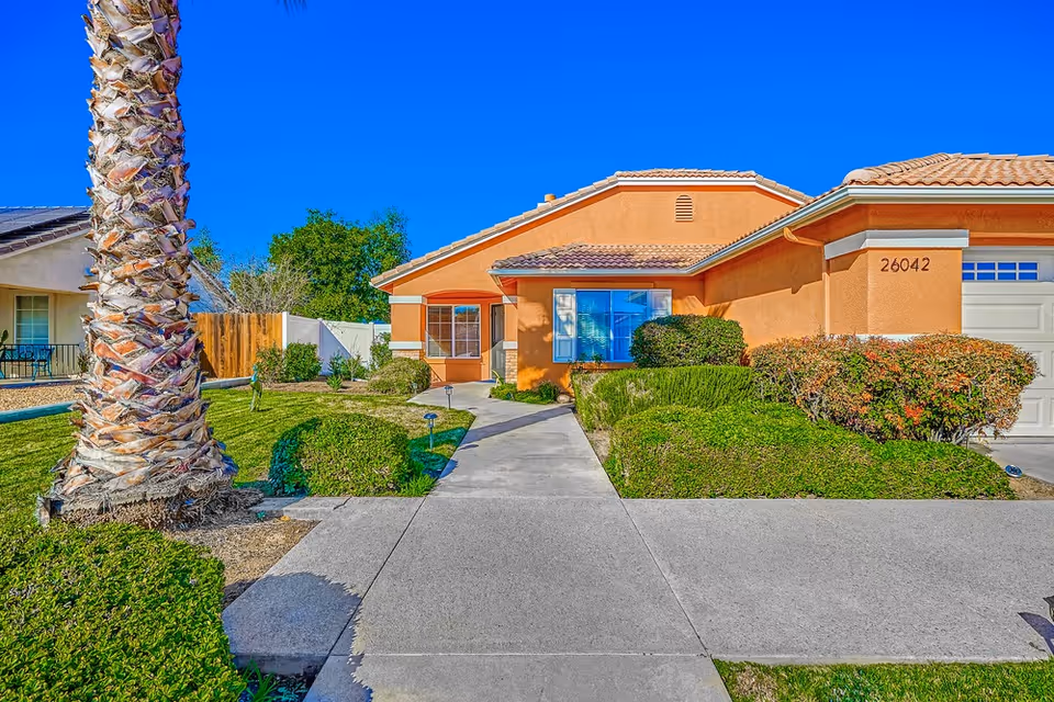 Orange single-story assisted living home with walkway, palm tree, and manicured front yard.